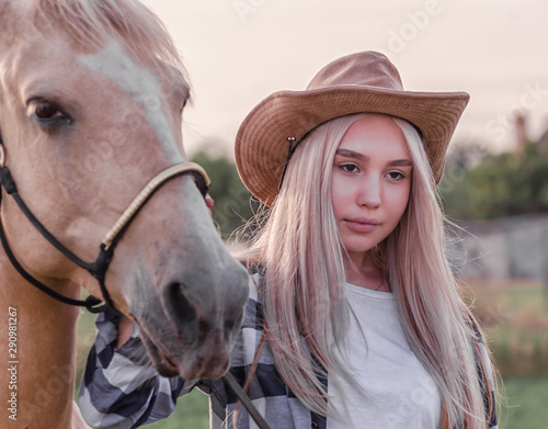 portrait of a young blonde girl dressed in a cowboy hat with a beige horse on a ranch close up