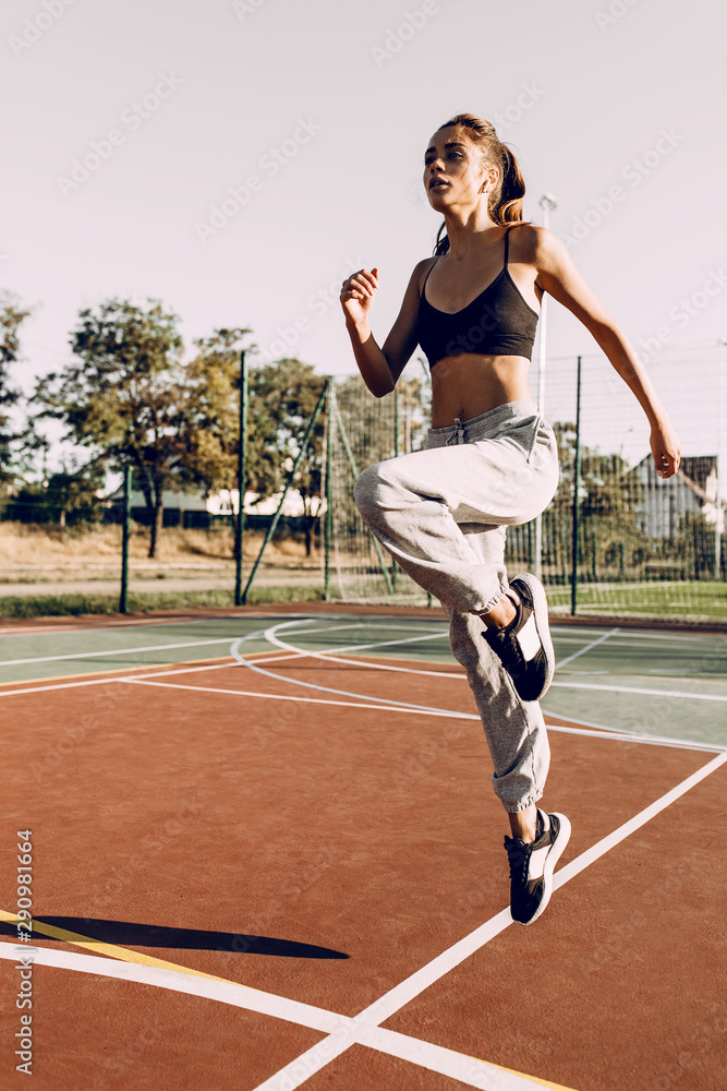 Attractive young girl sportswoman training outdoors, wearing headphones, doing jumps