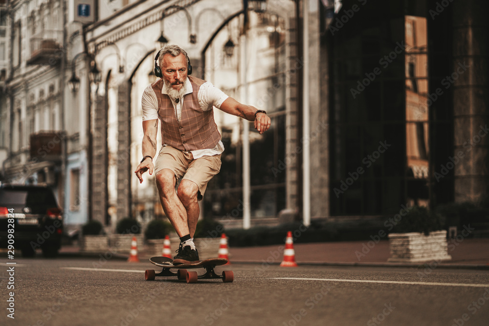 Portrait of handsome man in white shirt on sunset evening in summer. Stylish guy ride on skateboard on city street. Urban male lifestyle on buildings background Portrait of handsome man in white shirt on sunset evening in summer. Stylish guy ride on skateboard on city street. Urban male lifestyle on buildings background