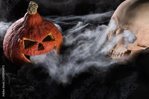 spooky human skull and carved Halloween pumpkin on black background