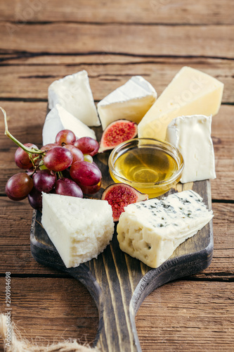 Various cheese, honey, grapes and figs on a wooden cutting board
