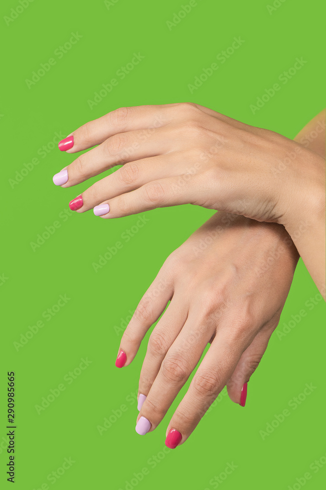 Woman demonstrating up two beautiful hands with trendy colorful manicure isolated on green background. Vertical color photography. Woman demonstrating up two beautiful hands with trendy colorful manicure isolated on green background. Vertical color photography.