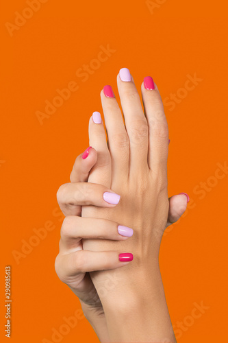 Woman rising up two beautiful hands with trendy colorful manicure isolated on green background. Vertical color photography.