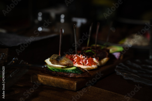 Sandwiches on skewers with different stuffing. With cucumber and herring, tomatoes, white cheese. Served on a wooden board. Horizontal orientation.