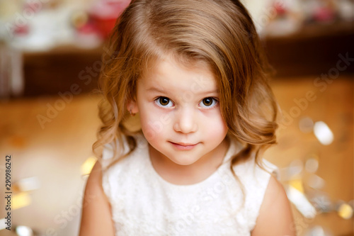 portrait of a happy cute girl of 4-5 years old in a white elegant dress in the New Year’s party waiting for a merry Christmas