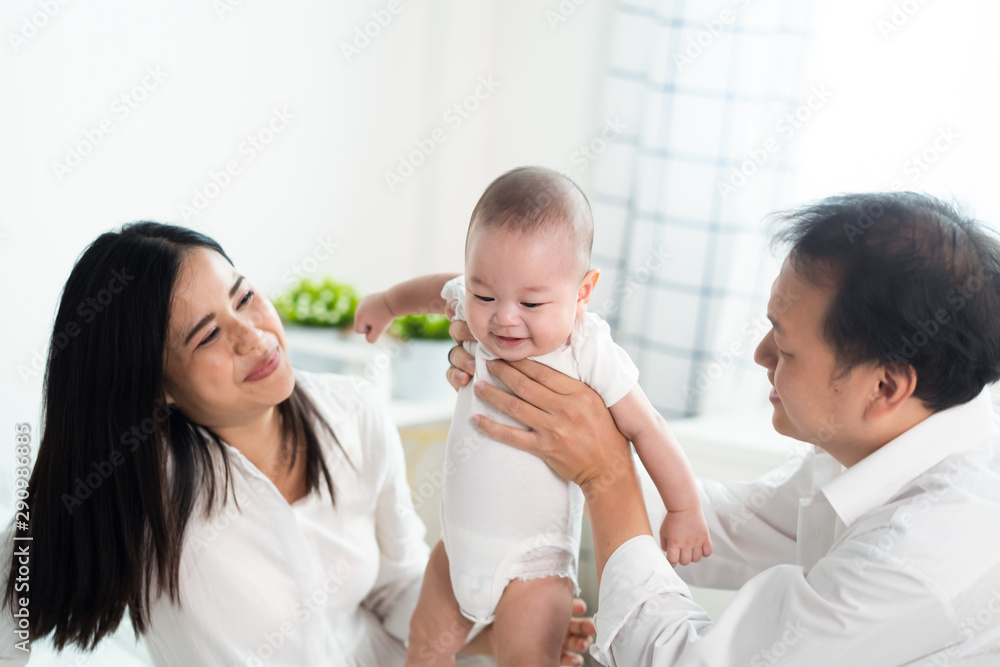 Asian parents holding and playing with newborn baby in bedroom. Father holding son in hand and Mother supporting the leg and smile to their child. Kid feeling happy with smile to be with family. Asian parents holding and playing with newborn baby in bedroom. Father holding son in hand and Mother supporting the leg and smile to their child. Kid feeling happy with smile to be with family.
