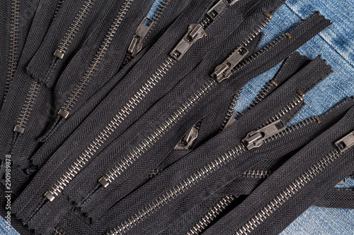 Pack a lot of black metal antique zippers stripes with sliders pattern for handmade sewing tailoring haberdashery leather craft on the blue denim background