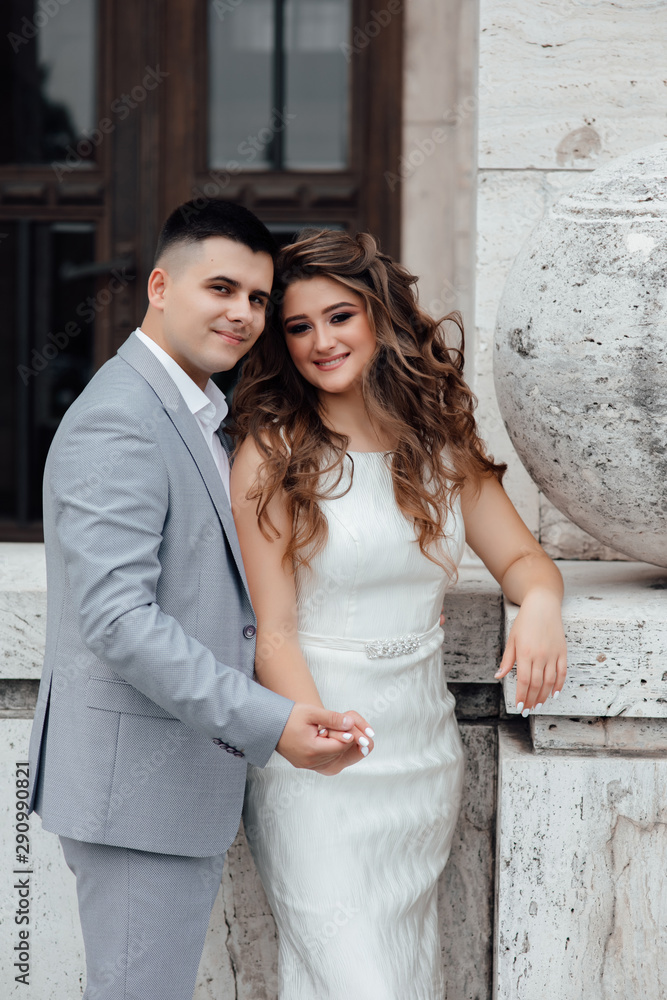 Stunning young couple. Family photo, romantic couple. Best time. Young man in grey suit embrase young wonderful woman in white dress
