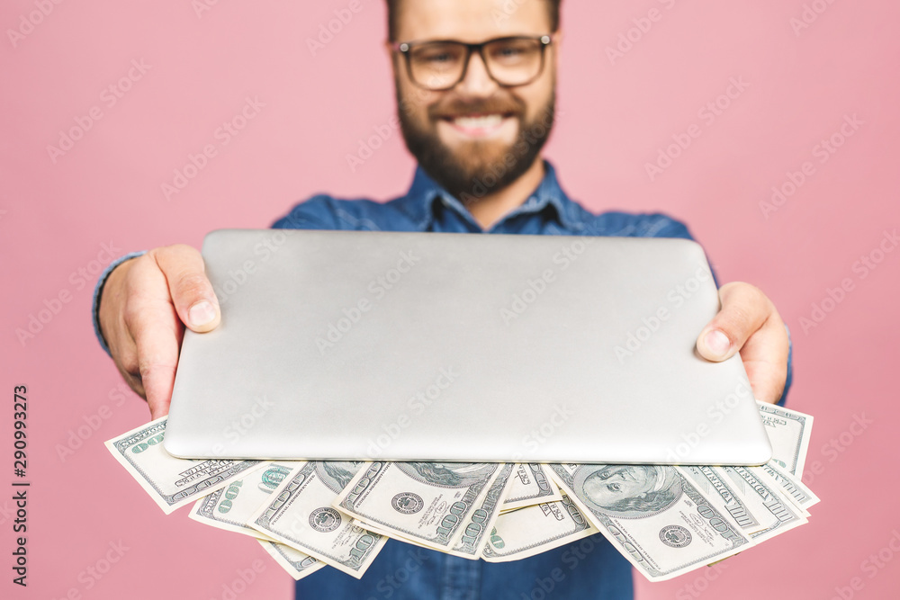 Happy winner! Portrait of excited casual man holding laptop and money isolated over pink background. Happy winner! Portrait of excited casual man holding laptop and money isolated over pink background.