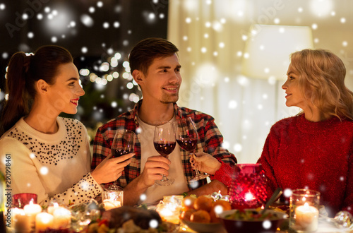 holidays and celebration concept - happy friends having christmas dinner at home, drinking red wine and clinking glasses over snow