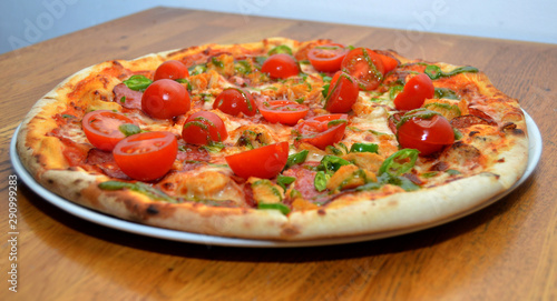 Close up of fresh baked pizza with cherry tomato, green peppers, pepperoni and mozzarella topping