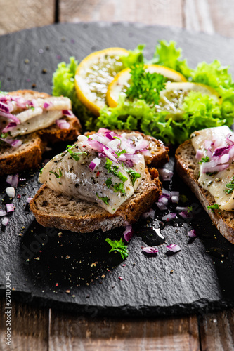 Marinated herring fillets on slices of bread on black stone