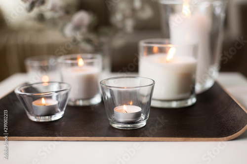 decoration, hygge and cosiness concept - burning white fragrance candles on tray table at cozy home
