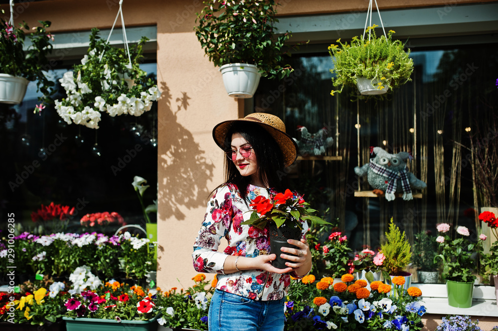 Summer portrait of brunette girl in pink glasses and hat against flowers shop.
