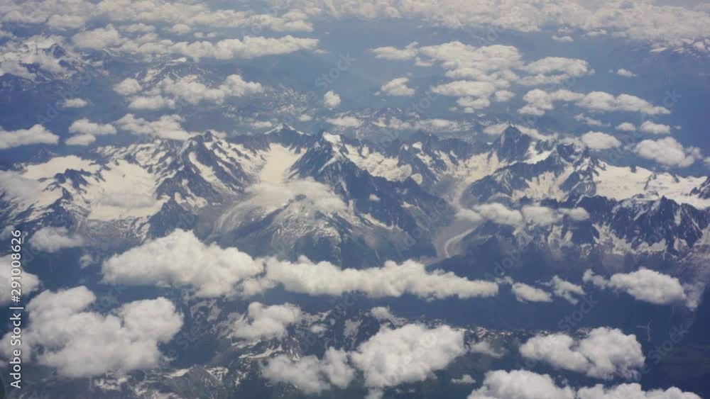 Summer snow-covered Alps view from the airplane window, the plane flies over the Alps mountains. Beautiful view from the porthole Summer snow-covered Alps view from the airplane window, the plane flies over the Alps mountains. Beautiful view from the porthole