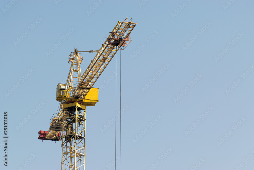 A yellow high-rise building crane against a blue sky builds multi-storey apartment buildings using modern technologies of metal, concrete and brick according to an architectural project