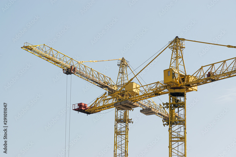 A yellow high-rise building crane against a blue sky builds multi-storey apartment buildings using modern technologies of metal, concrete and brick according to an architectural project