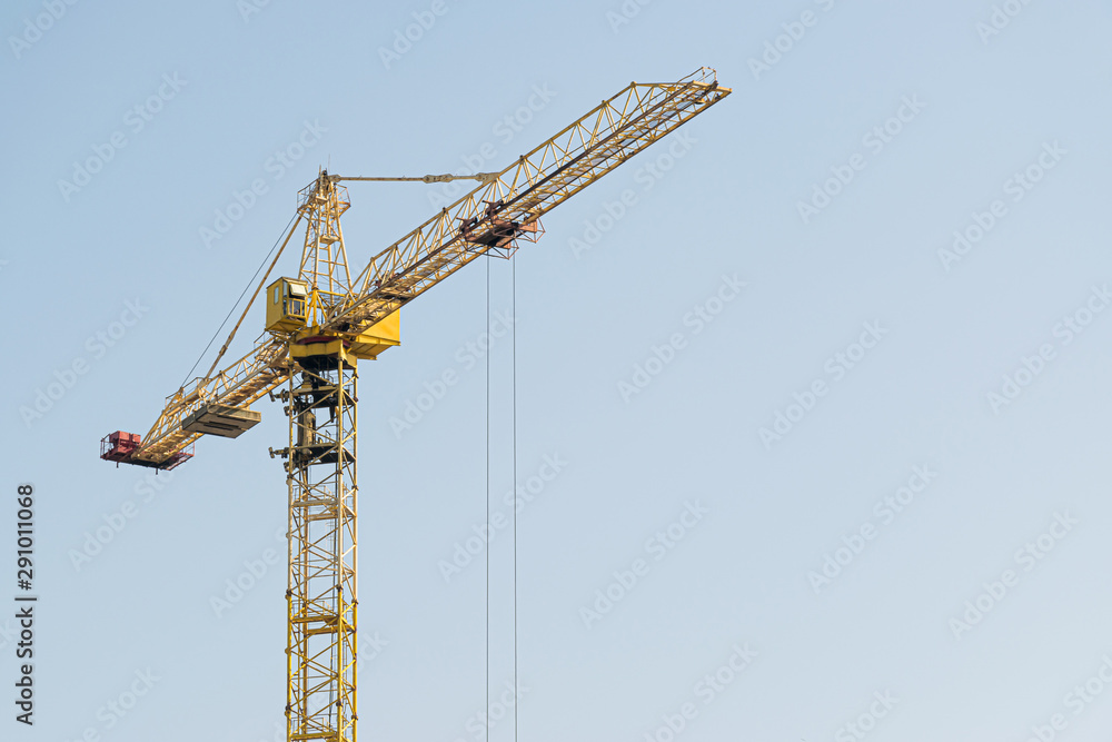 A yellow high-rise building crane against a blue sky builds multi-storey apartment buildings using modern technologies of metal, concrete and brick according to an architectural project