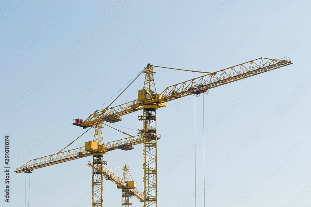 A yellow high-rise building crane against a blue sky builds multi-storey apartment buildings using modern technologies of metal, concrete and brick according to an architectural project