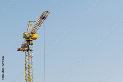 A yellow high-rise building crane against a blue sky builds multi-storey apartment buildings using modern technologies of metal, concrete and brick according to an architectural project