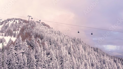 Aerial view over snowy mountain forest valley with clouds, cable car lifting. Outdoor snow alpine wild natural ski resort. Transportation in winter. High altitude gondola in winter. Ski Gondola photo