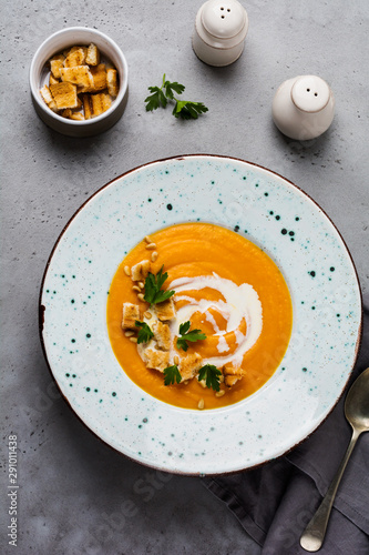 Pumpkin soup with cream, pieces of bread and cedar nuts in black ceramic plate on gray concrete background. Traditional autumn food. Top view copy space.