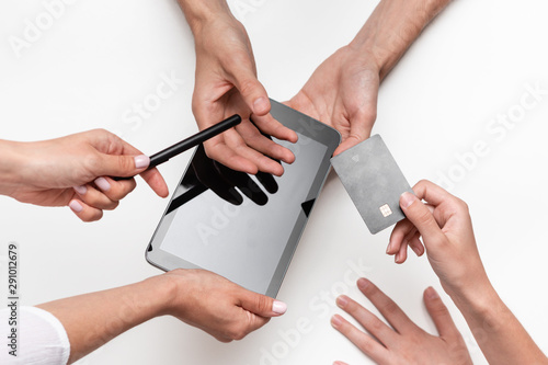 Close up top view of a woman hands over bank card to a man in order to pay for the product. Tablet and pen on a white table. Concept of e-commerce and online shopping. Successful deal.
