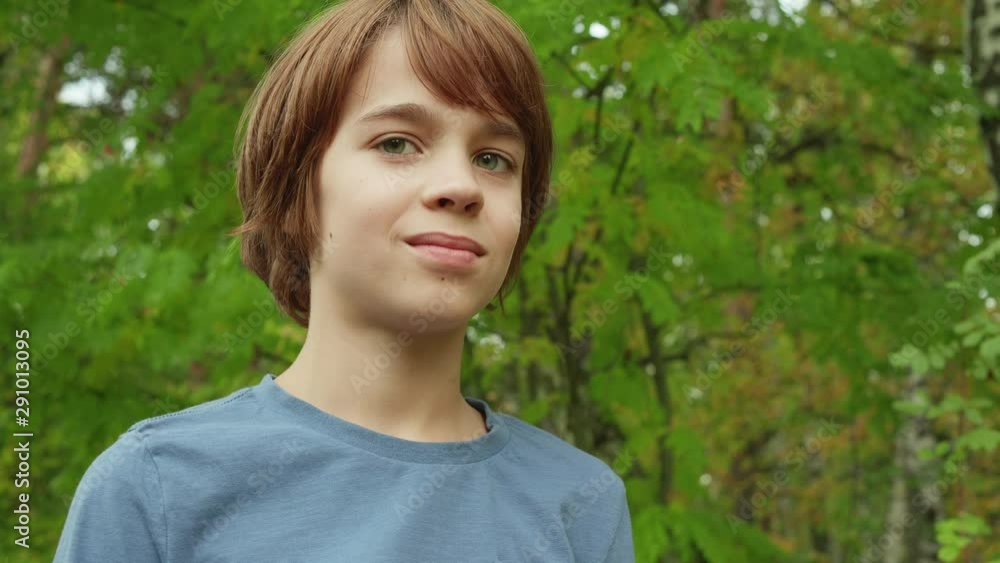 Portrait teenager boy looking to camera on green foliage background. Handsome young boy posing to camera on summer trees background in city park Portrait teenager boy looking to camera on green foliage background. Handsome young boy posing to camera on summer trees background in city park