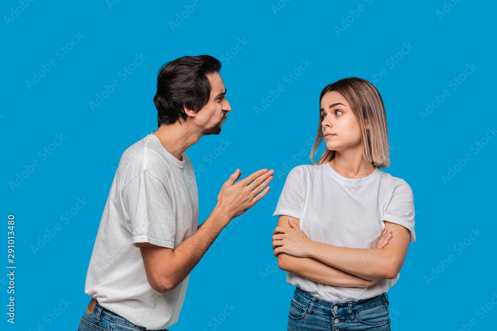 Brunet bearded man with mustaches in white t-shirt and blue jeans asking his girlfriend for forgiveness isolated over blue background. Concept of guilt. Brunet bearded man with mustaches in white t-shirt and blue jeans asking his girlfriend for forgiveness isolated over blue background. Concept of guilt.