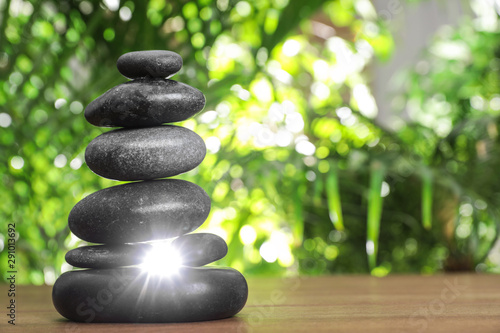 Table with stack of stones and blurred green leaves on background  space for text. Zen concept