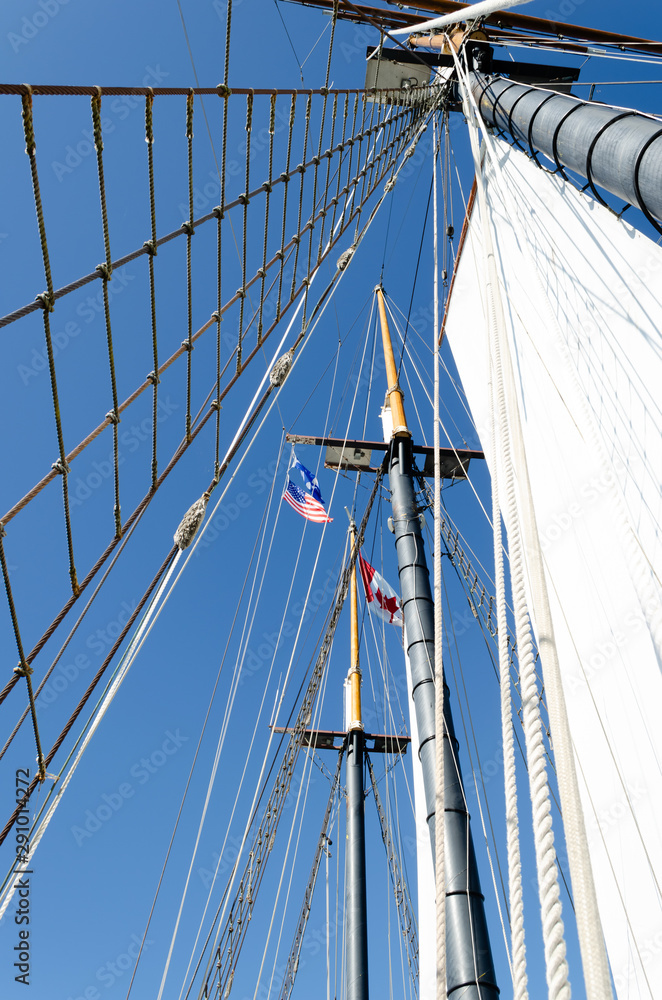 Obraz premium Skyward view of three Tall Ship masts and sails showing Canada and USA flags