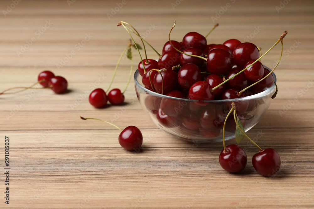 Glass bowl of delicious cherries on wooden table, space for text Glass bowl of delicious cherries on wooden table, space for text