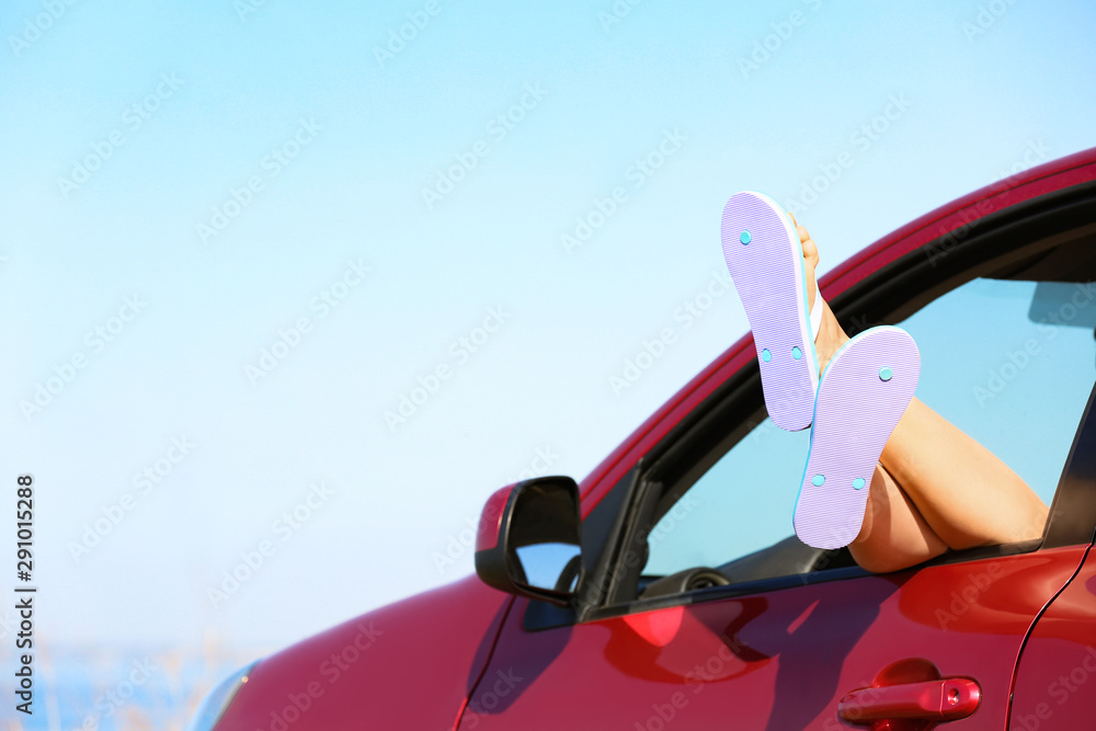Closeup of woman showing legs with flip flops from car, space for text. Beach accessories