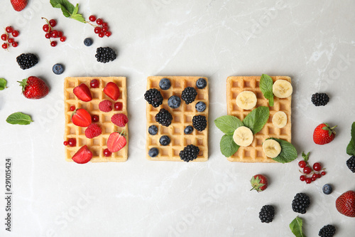 Flat lay composition with delicious waffles and fresh berries on light marble table