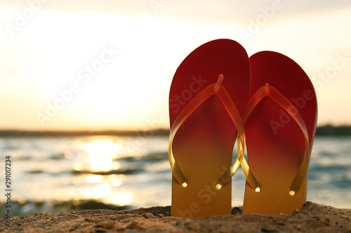 Stylish flip flops on sand near sea  space for text. Beach accessories