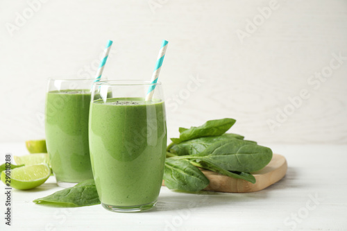 Glasses of healthy green smoothie with fresh spinach on white wooden table against light background. Space for text