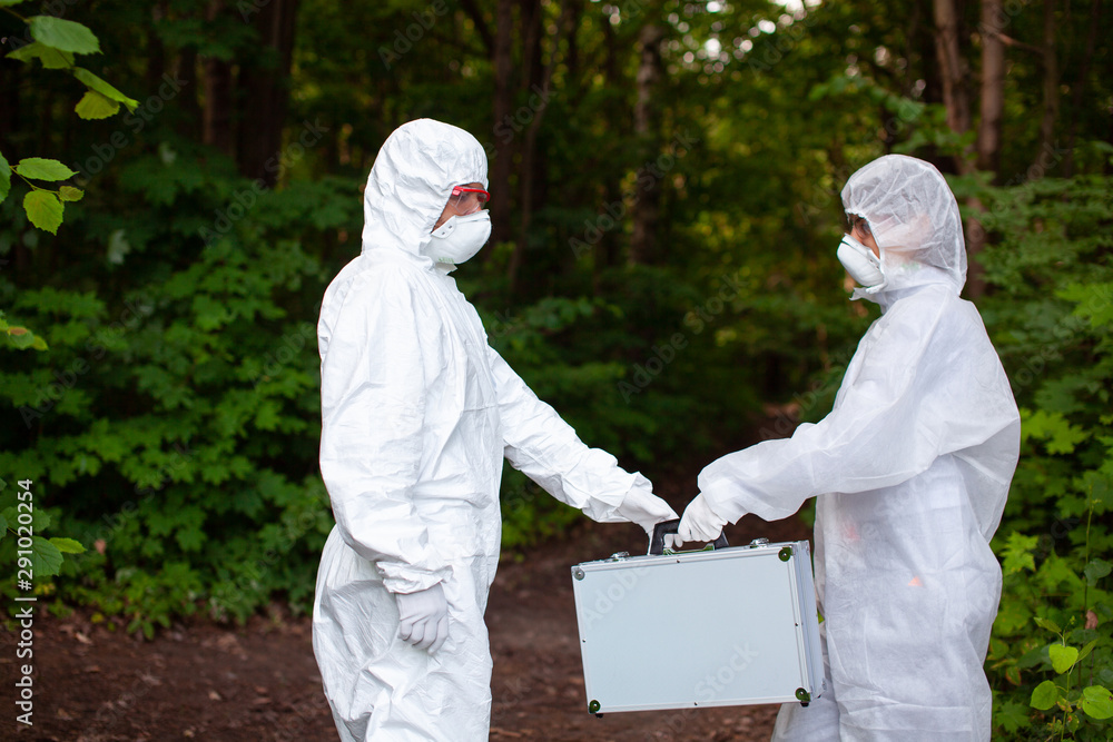 Ecological problem. Pollution. Examine soil. Scientist working in forest in protective mask and suit taking water and soil samples. Chemist makes an analysis of the environment for radiation. Ecological problem. Pollution. Examine soil. Scientist working in forest in protective mask and suit taking water and soil samples. Chemist makes an analysis of the environment for radiation.