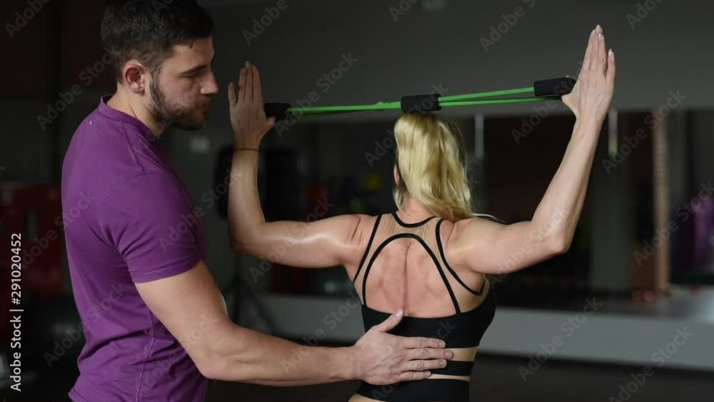 Fit young woman training with expander, working out in a gym with personal trainer assistance cheering her on. Personal training and bodybuilding concept Fit young woman training with expander, working out in a gym with personal trainer assistance cheering her on. Personal training and bodybuilding concept