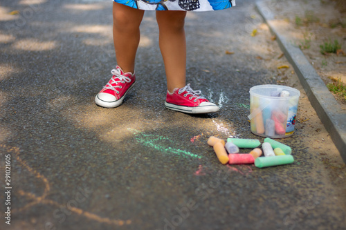 child drawing with chalk on asphalt. boy playing alone in the street. holding a piece of chalk in his fingers