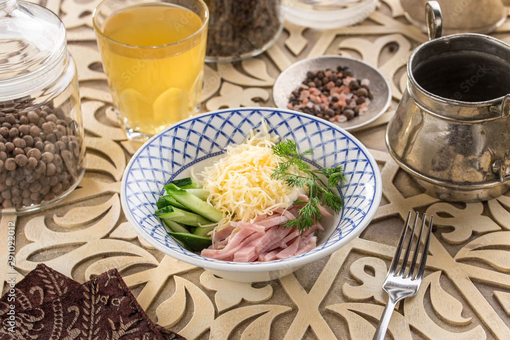 Fresh salad with cucumber, cheese and ham and glass of lemonade on oriental wooden table Fresh salad with cucumber, cheese and ham and glass of lemonade on oriental wooden table