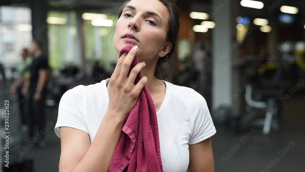 Portrait of young fitness woman wipes sweat from her forehead with a towel when posing in gym. European caucasian female model in sportswear. Portrait of young fitness woman wipes sweat from her forehead with a towel when posing in gym. European caucasian female model in sportswear.
