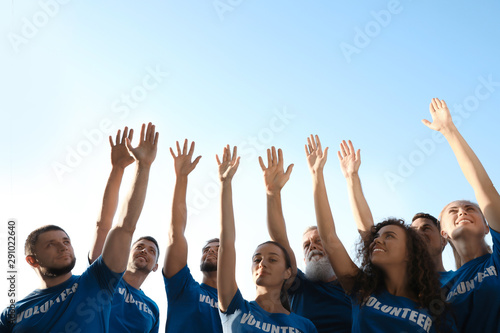 Group of volunteers raising hands outdoors on sunny day