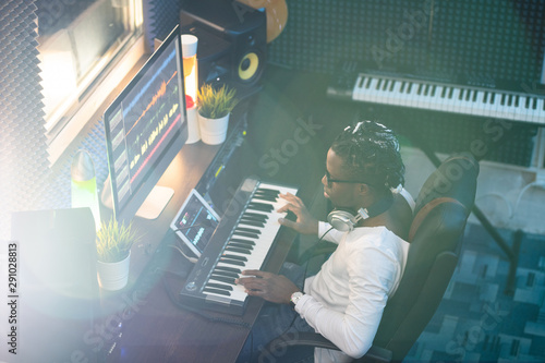 Young African musician in casualwear looking at computer screen by workplace photo