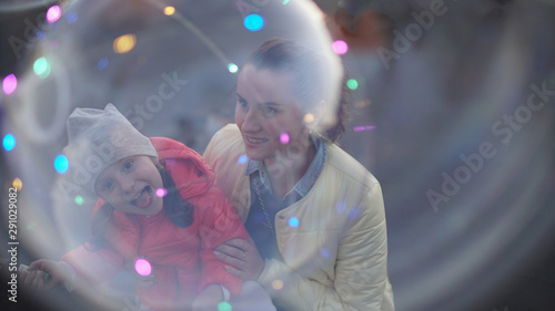 Smiling young mother and happy daughter behind big soap bubble.