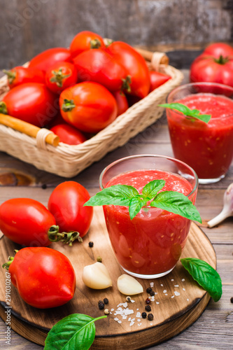 Fresh tomato juice with basil leaves in glasses and tomatoes on a wooden table