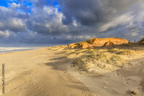 Beautiful sunrise on the beach and dunes Dutch North Sea coast illuminated by warm light from the first sunbeams against the tops of the dunes and a heavily clouded sky