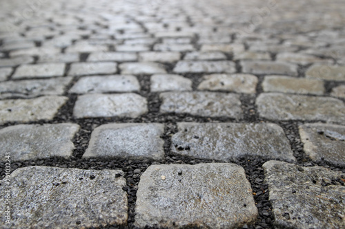 An old stoneblock pavement cobbled with rectangular granite blocks with crushed rock fines between blocks. Photo in perspective with selective focus
