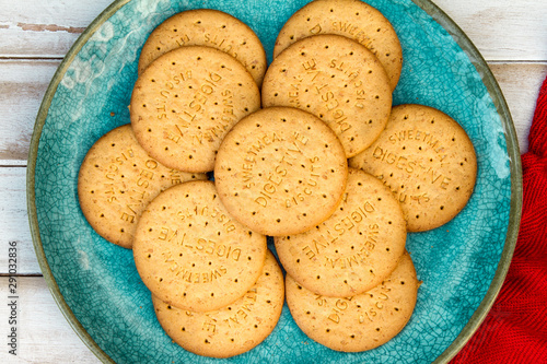 Round digestive biscuits on a turquoise plate on a white wooden table with a red cloth photo