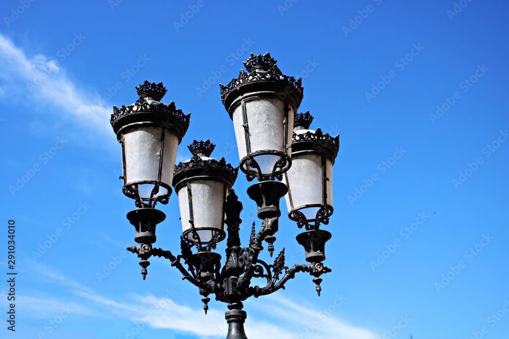 Beautiful old metal street lamp post with four lamps on a blue sky background Beautiful old metal street lamp post with four lamps on a blue sky background