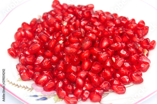 Pomegranate seeds placed in a plate with scattered seeds on white background